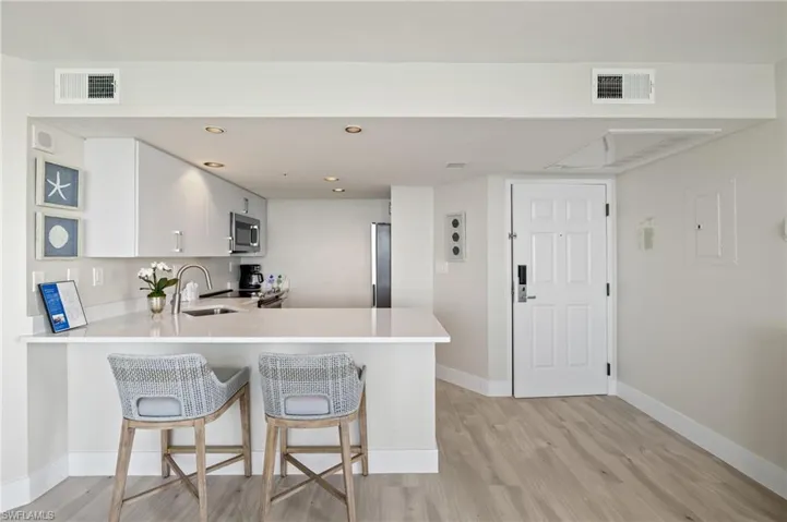 Kitchen featuring white cabinetry, sink, light hardwood / wood-style flooring, kitchen peninsula, and a kitchen bar