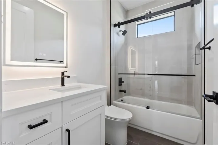 Full bathroom with wood-type flooring, shower / bath combination with glass door, vanity, and toilet