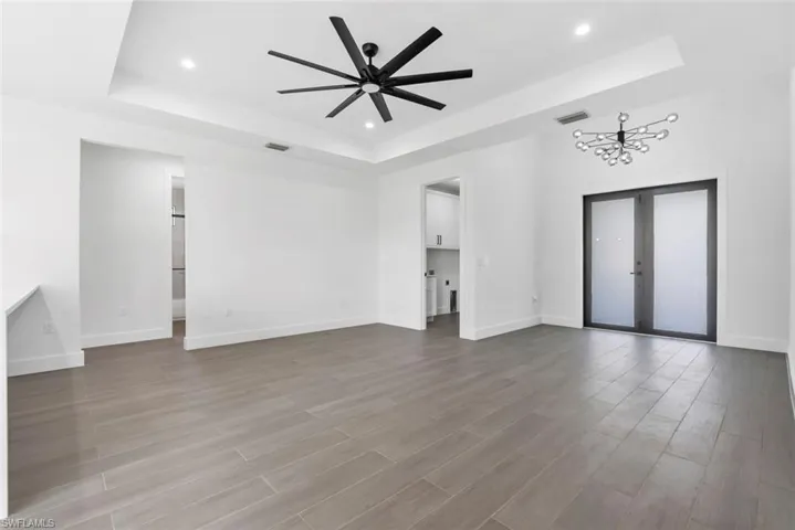 Unfurnished living room featuring tile flooring, ceiling fan with notable chandelier, a raised ceiling, and french doors