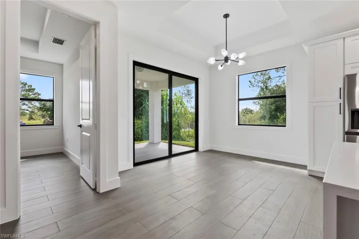Spare room featuring a raised ceiling, light hardwood / wood-style flooring, plenty of natural light, and a chandelier