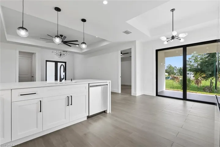 Kitchen with white cabinets, a raised ceiling, sink, stainless steel dishwasher, and ceiling fan with notable chandelier
