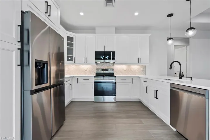 Kitchen with appliances with stainless steel finishes, white cabinetry, backsplash, decorative light fixtures, and sink