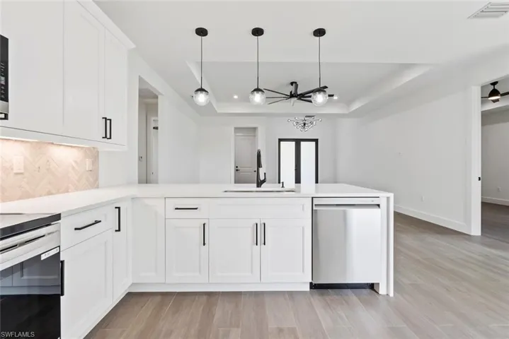 Kitchen featuring white cabinets, sink, light hardwood / wood-style flooring, appliances with stainless steel finishes, and a tray ceiling
