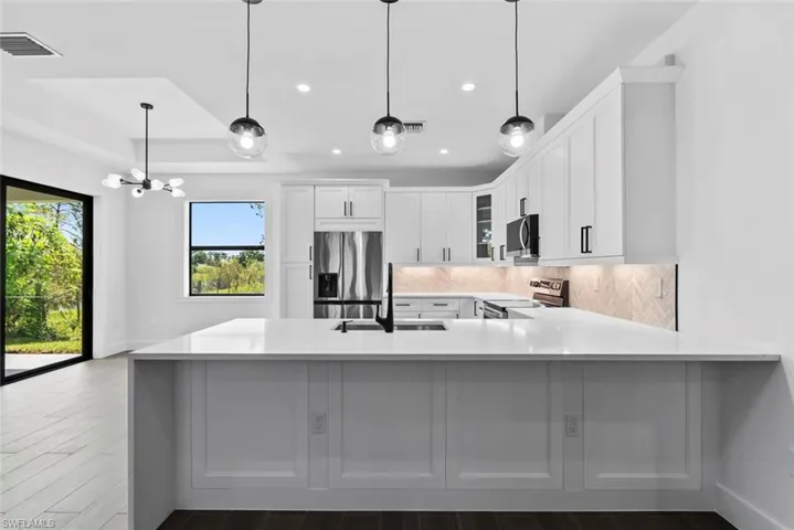 Kitchen featuring stainless steel appliances, white cabinets, kitchen peninsula, and hanging light fixtures