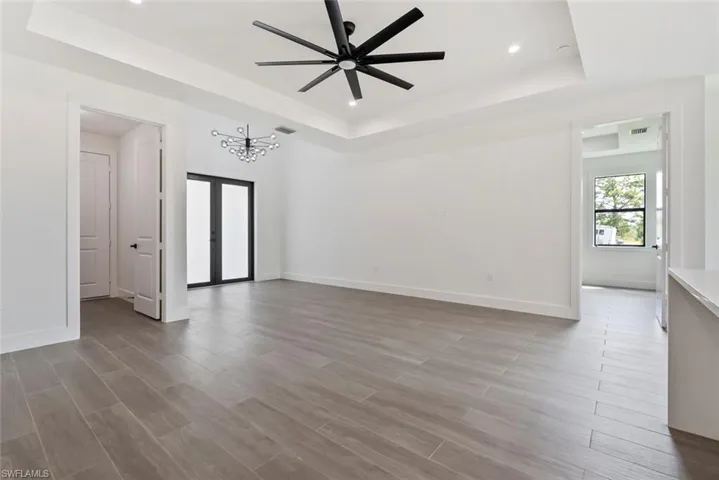Empty room with light hardwood / tile flooring, a raised ceiling, and ceiling fan with notable chandelier