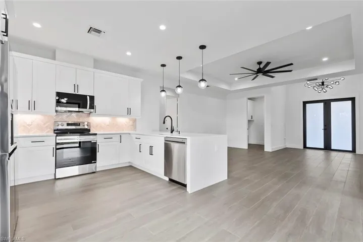 Kitchen featuring white cabinets, ceiling fan with notable chandelier, kitchen peninsula, pendant lighting, and stainless steel appliances