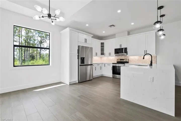 Kitchen with sink, white cabinetry, hanging light fixtures, stainless steel appliances, and light stone countertops