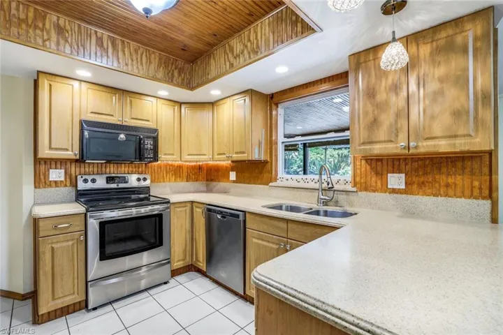 Kitchen with a tray ceiling, pendant lighting, light countertops, appliances with stainless steel finishes, and a sink
