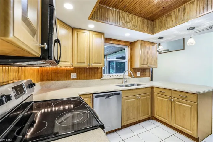 Kitchen featuring decorative light fixtures, stainless steel appliances, a raised ceiling, light countertops, and a sink