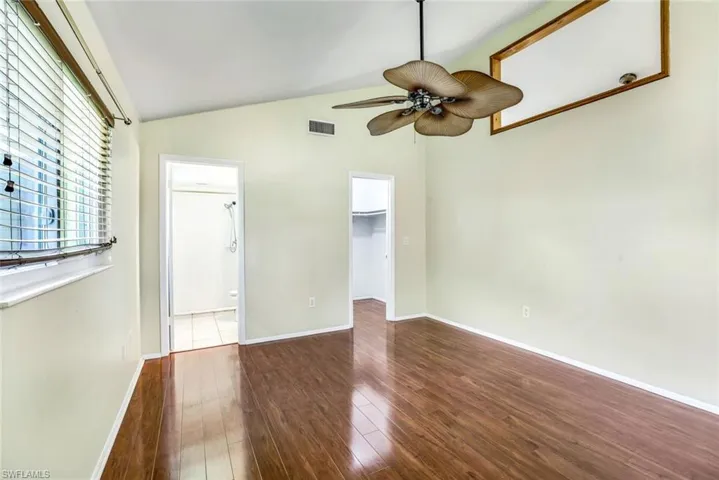 Unfurnished bedroom featuring dark wood-style floors, a spacious closet, vaulted ceiling, and baseboards