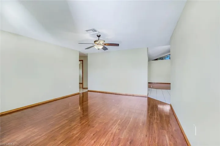Unfurnished room featuring a ceiling fan, visible vents, baseboards, and wood finished floors