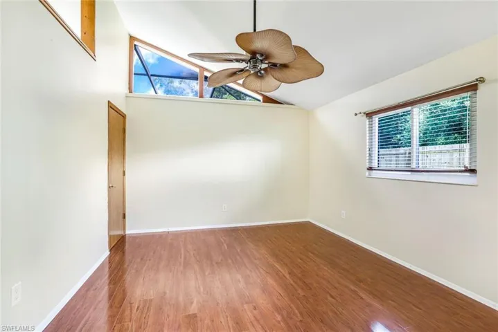 Spare room with vaulted ceiling, wood finished floors, a wealth of natural light, and baseboards
