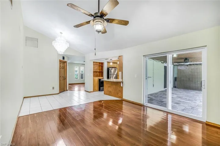 Unfurnished living room with light wood-type flooring, visible vents, vaulted ceiling, and ceiling fan with notable chandelier