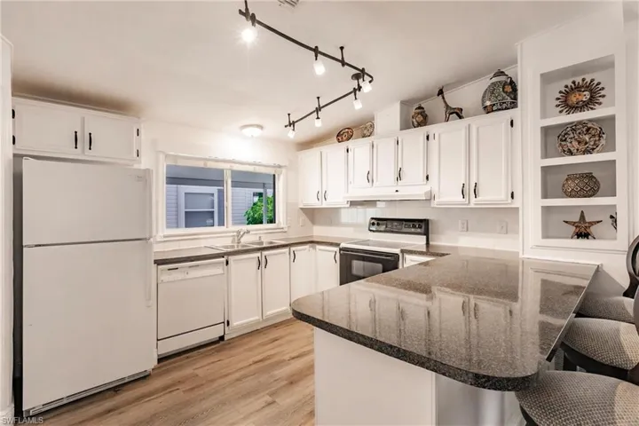 Kitchen with a sink, white appliances, a peninsula, white cabinetry, and under cabinet range hood