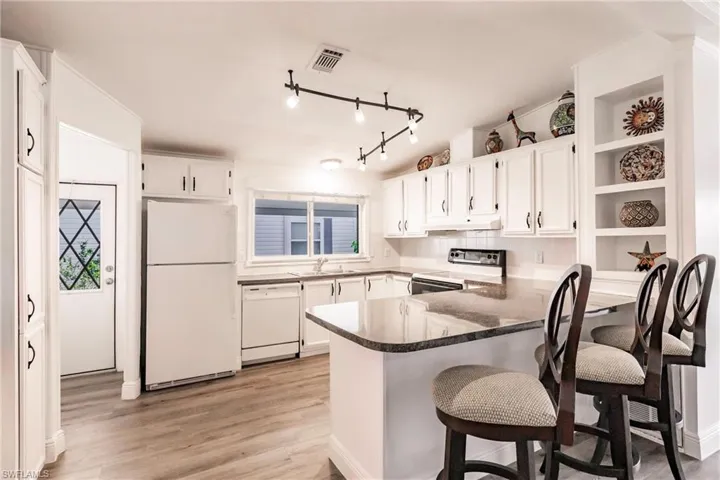 Kitchen with lots of storage, open display shelves, a breakfast bar, under cabinet range hood, and white appliances