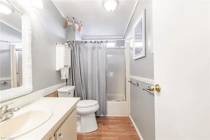Bathroom with crown molding, laminate floors and shower / tub combo with glass door and decorative shower curtain