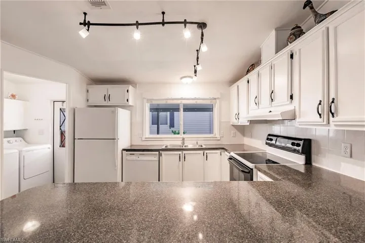 Kitchen featuring washer and dryer, a sink, white appliances, white cabinetry, and under cabinet range hood