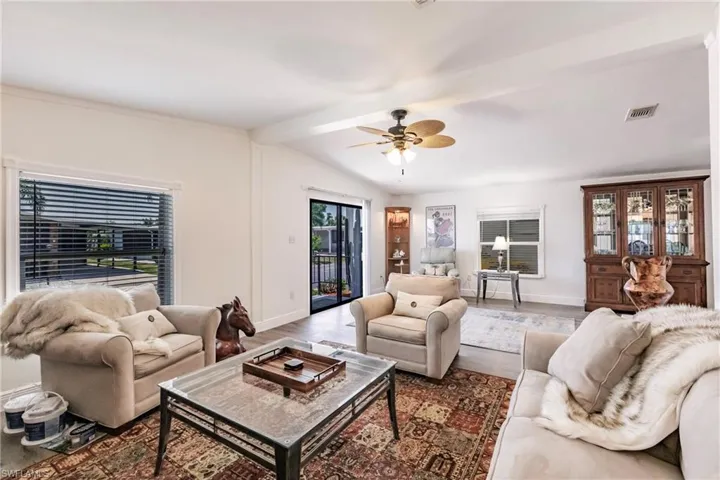 Living area featuring laminate floors, ceiling fan and lofted ceiling with beams