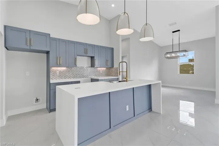 Kitchen featuring backsplash, a center island with sink, hanging light fixtures, and sink