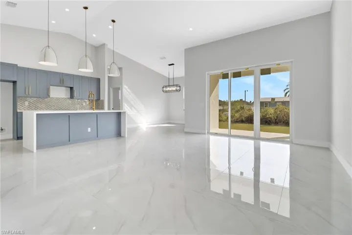 Kitchen featuring decorative light fixtures, decorative backsplash, vaulted ceiling, and a kitchen island with sink