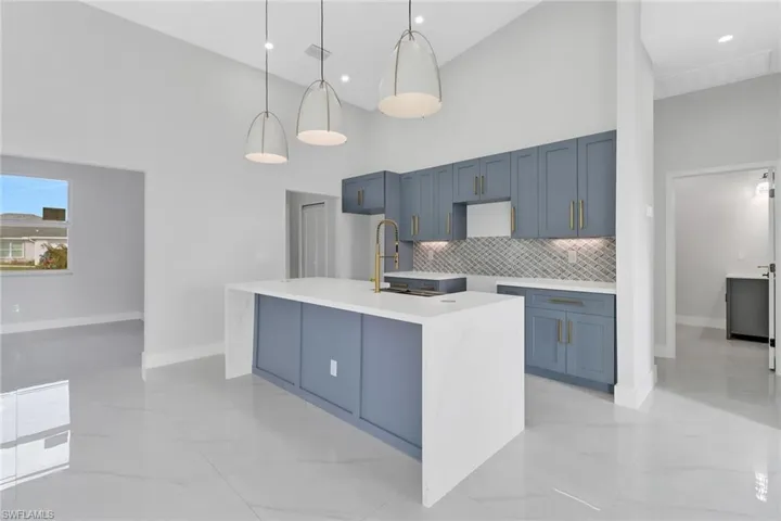Kitchen with hanging light fixtures, a kitchen island with sink, a high ceiling, and tasteful backsplash