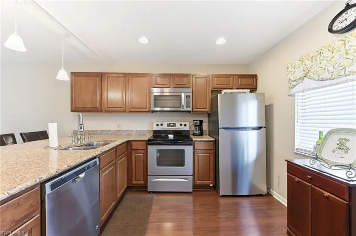 Kitchen with stainless steel appliances, updated wood cabinets, quartz countertop, hardwood flooring, and recessed lighting
