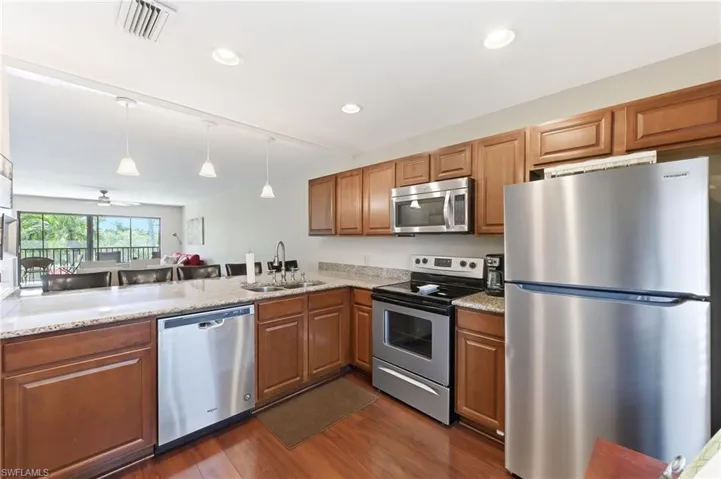 Kitchen with stainless steel appliances, quartz counters, hanging light fixtures, and wood finish cabinets
