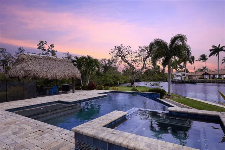 Pool at dusk with a patio, a water view, and a pool with connected hot tub