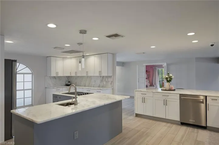 Kitchen with a center island with sink, visible vents, white cabinets, decorative backsplash, and dishwasher