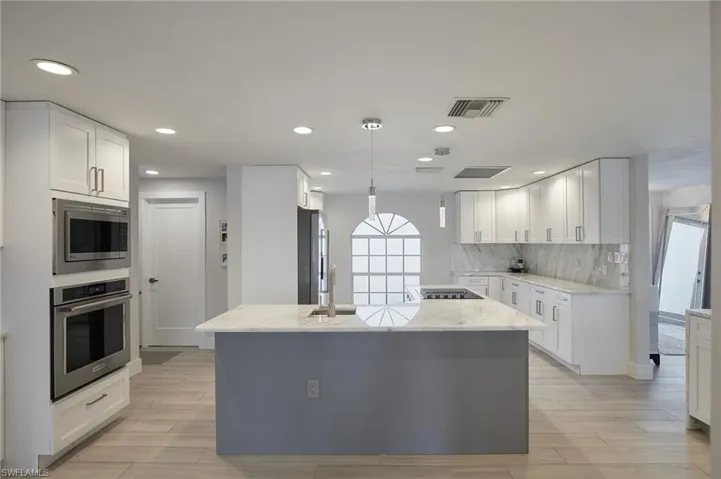 Kitchen with visible vents, decorative backsplash, appliances with stainless steel finishes, light stone countertops, and white cabinetry