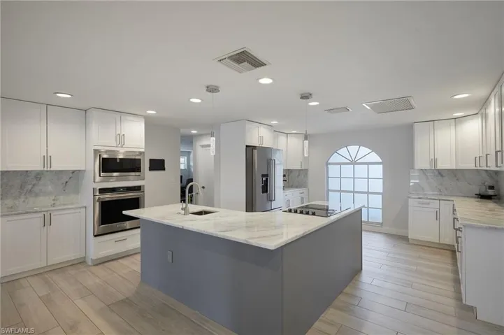 Kitchen with a kitchen island with sink, stainless steel appliances, a sink, visible vents, and white cabinets