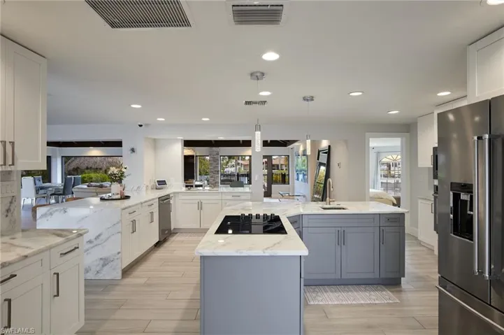 Kitchen with high end fridge, visible vents, a center island with sink, and black electric cooktop