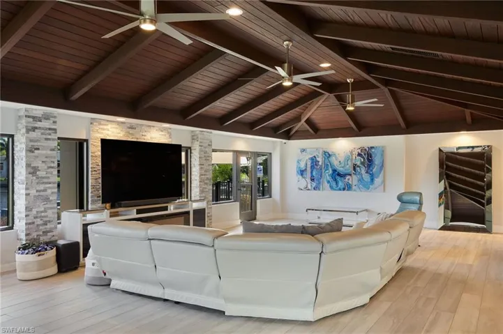 Living room with lofted ceiling with beams, wood ceiling, a ceiling fan.