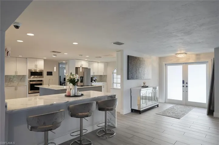 Kitchen with french doors, a center island with sink, stainless steel appliances, tasteful backsplash, and light stone countertops