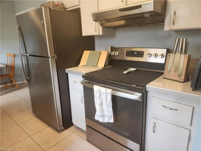 Kitchen with stainless steel appliances, light countertops, white cabinetry, and light tile patterned floors