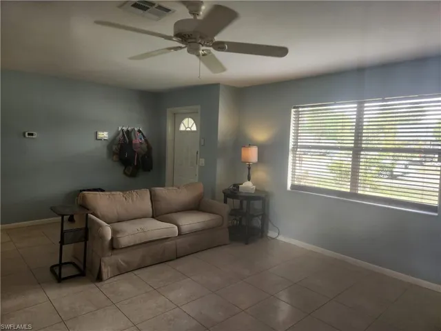 Tiled living area with a ceiling fan and baseboards