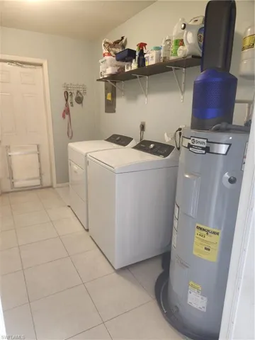 Laundry area featuring water heater, light tile patterned floors, washer and dryer, and door leading to the backyard.