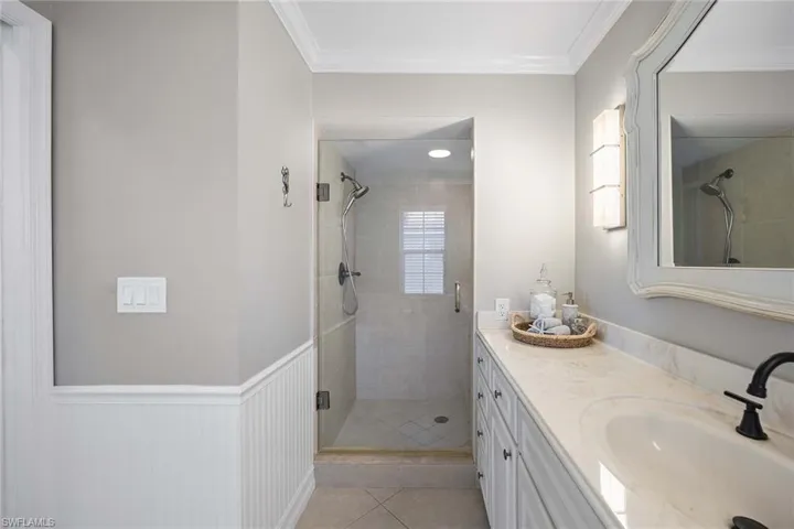 Full bathroom featuring vanity, a shower stall, wainscoting, crown molding, and light tile patterned flooring