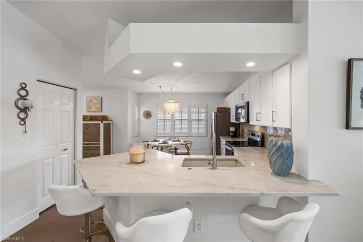 Kitchen with a peninsula, a breakfast bar area, stainless steel appliances, white cabinetry, and dark wood finished floors