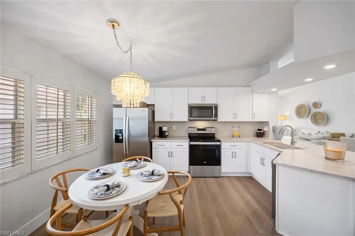 Kitchen featuring stainless steel appliances, lofted ceiling, a chandelier, light stone counters, and white cabinetry