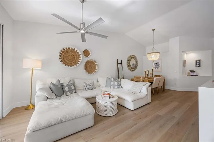 Living room featuring light wood-type flooring, vaulted ceiling, a ceiling fan, and a chandelier
