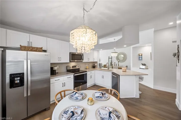 Kitchen featuring stainless steel appliances, a chandelier, white cabinetry, pendant lighting, and a peninsula