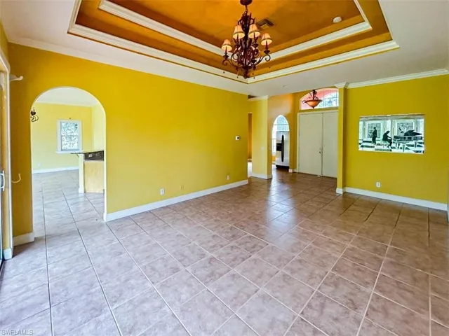 Tiled spare room with a chandelier, ornamental molding, a healthy amount of sunlight, and a tray ceiling