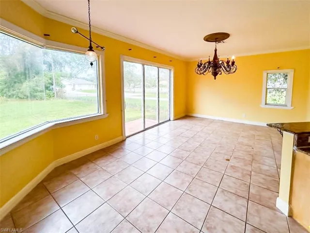 Unfurnished dining area with light tile patterned flooring, an inviting chandelier, a healthy amount of sunlight, and crown molding