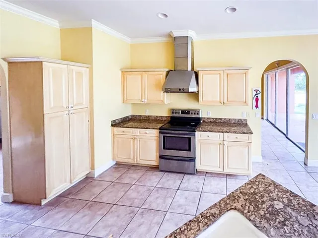 Kitchen with crown molding, stainless steel range with electric stovetop, light tile patterned floors, and wall chimney range hood