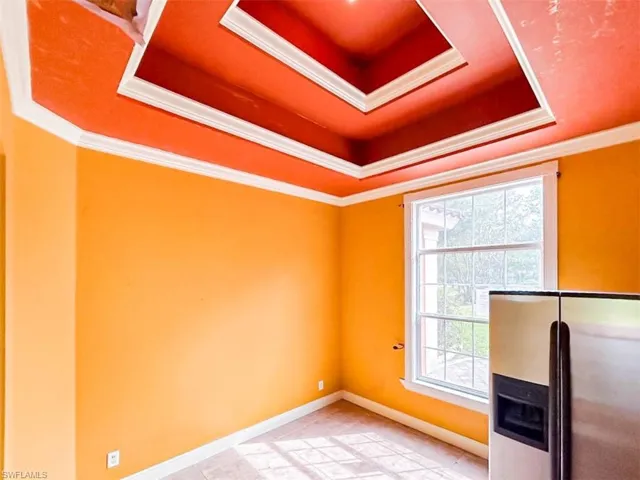 Empty room featuring a tray ceiling, light tile patterned floors, and ornamental molding