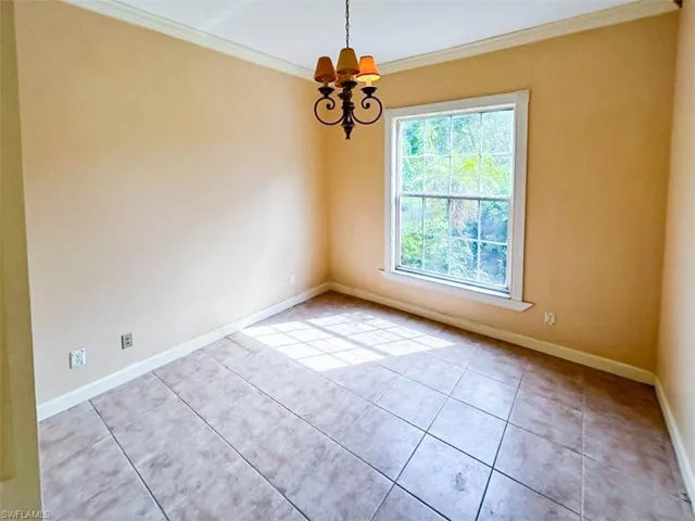 Tiled spare room with a notable chandelier and ornamental molding