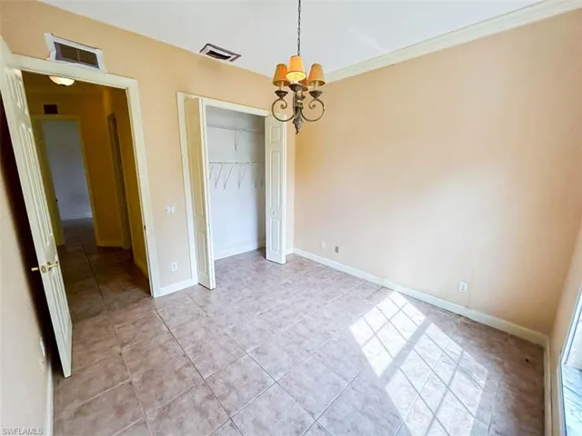 Unfurnished bedroom with light tile patterned floors, a chandelier, a closet, and crown molding