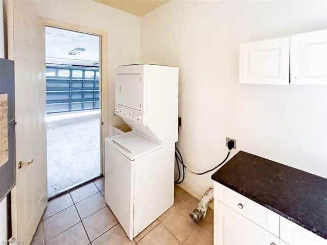 Laundry room with stacked washer / dryer, cabinets, and light tile patterned floors