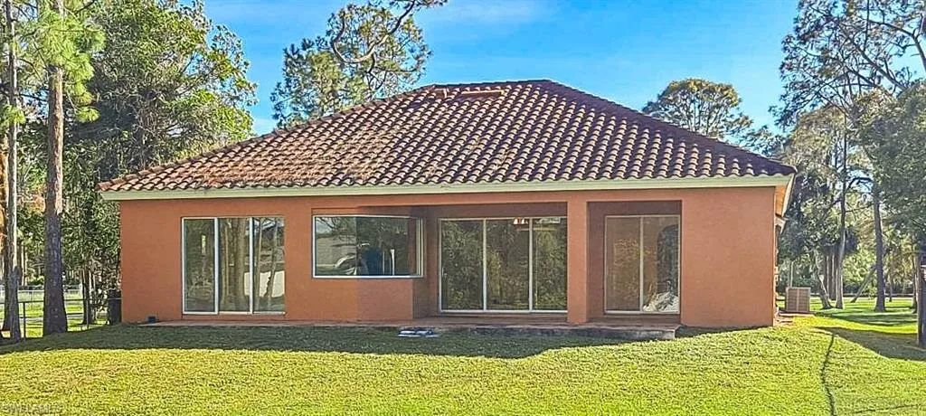 Back of house with central AC unit and a lawn